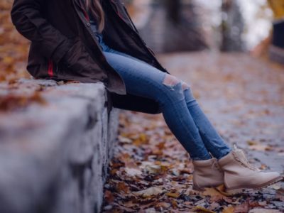 a girl wearing ripped jeans and booties sits outside during the fall