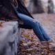 a girl wearing ripped jeans and booties sits outside during the fall