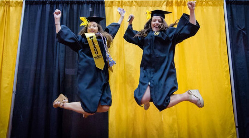 Mizzou graduates jump in the air in their caps and gowns.