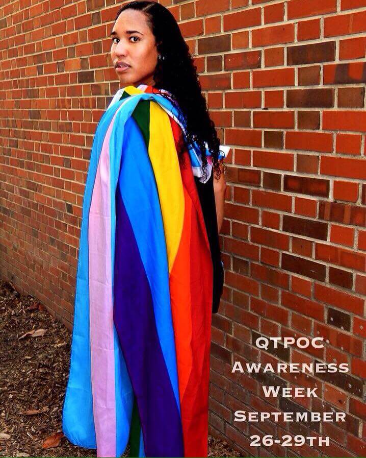 Ellie Gaustria, president of QTPOCU, poses with the gay pride and transgender pride flags draped over her shoulder.