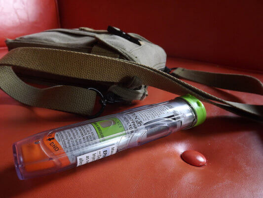 An EpiPen rests on a couch next to a messenger bag.