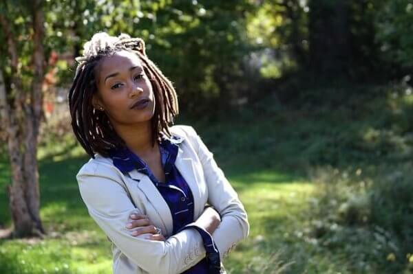 A businesswoman with dreadlocks looks forward.