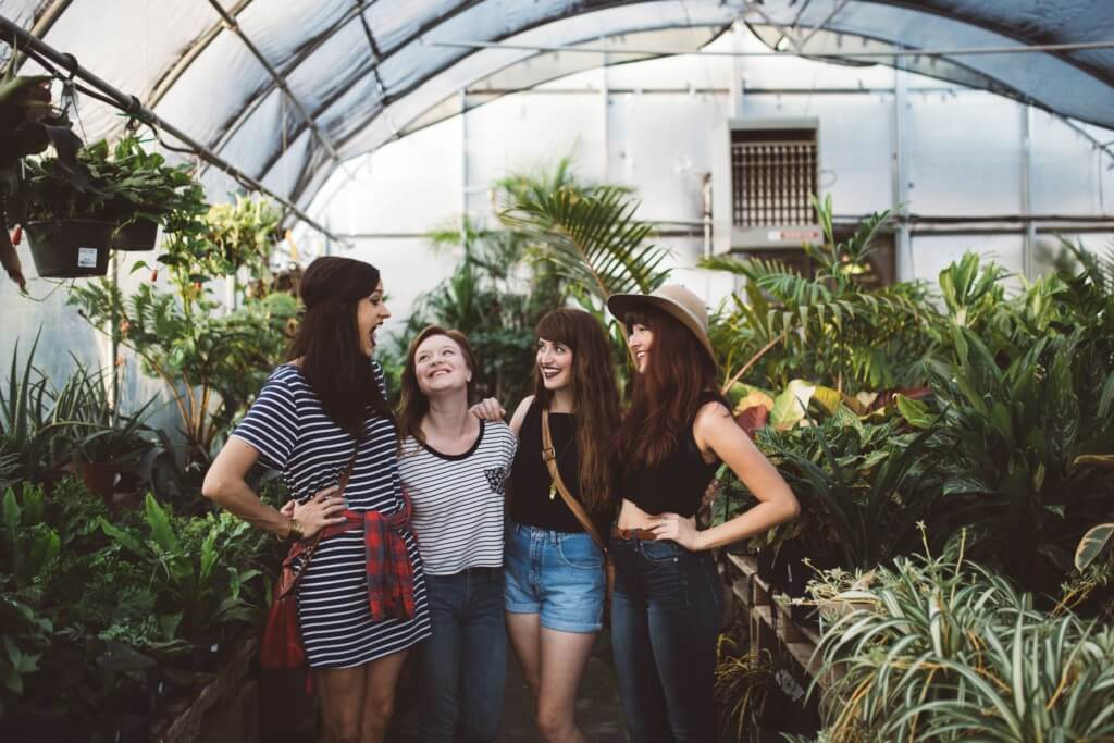 four girl friends laughing in a green house