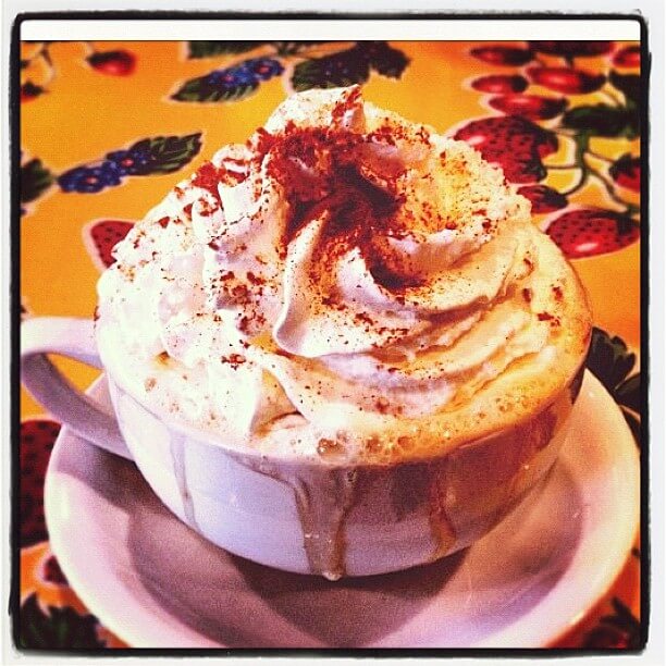 A cup of pumpkin latte overflowing with whipped cream topped with cinnamon from a gainesville breakfast place