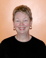 This picture shows Kickie Britt smiling against a peach background in a black shirt and red earrings.