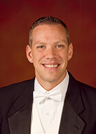 This picture shows Prof. Shawn Vondran from Northwestern Bienen School of Music smiling in a black suit and white bowtie against a red background.