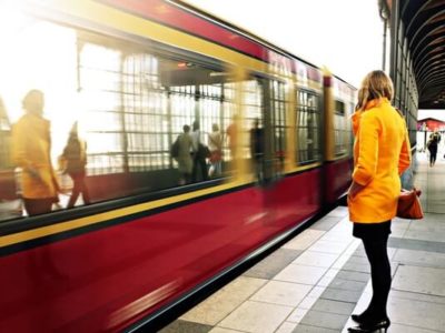 Girl in yellow coat watching as a subway whizzes by commuting