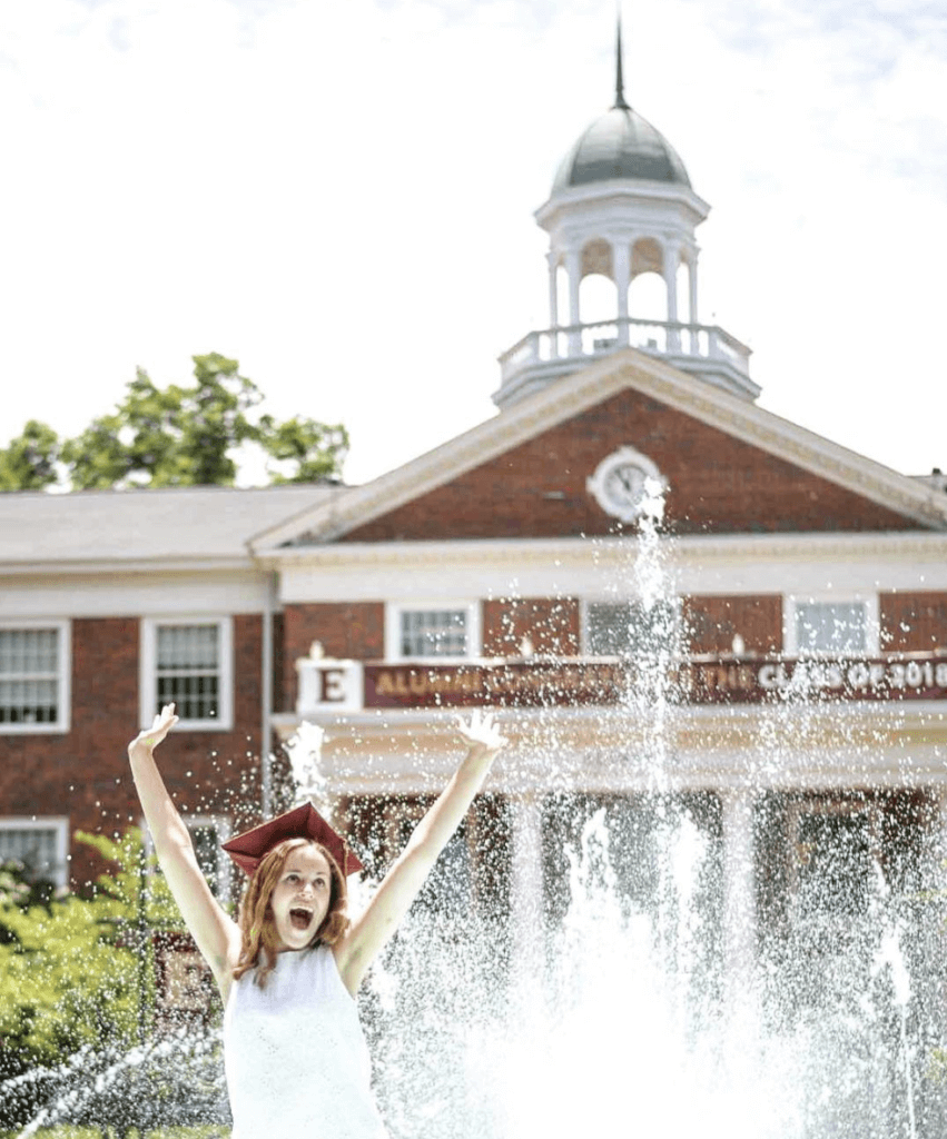 elon university grad in front of fountain