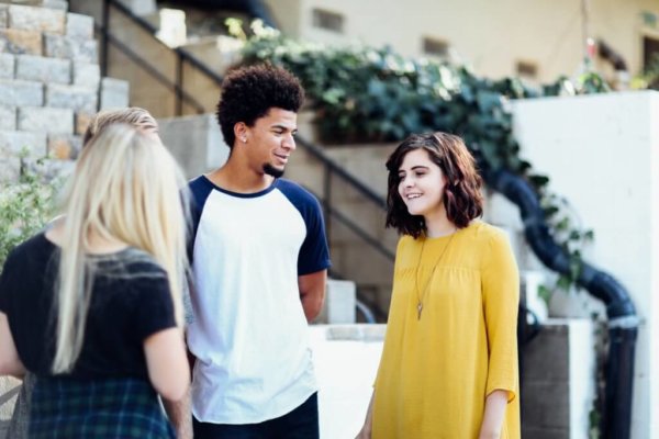 two girls and one boy talk to each other in front of some stairs