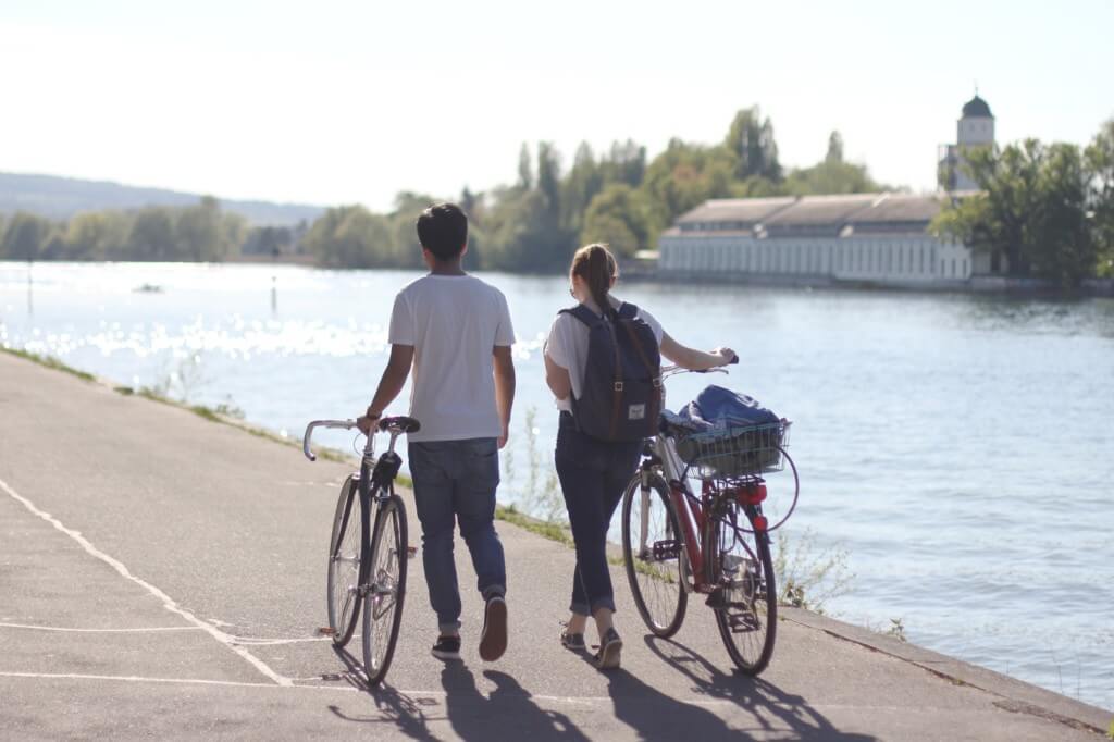 boy and girl walk their bicycles together along a riverbank