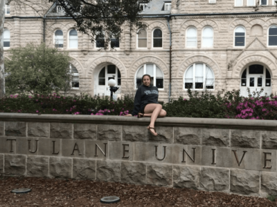 girl in a Tulane hoodie sitting on the sign that says 