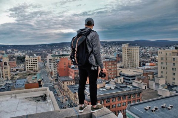 man standing on rooftop edge overlooking a city