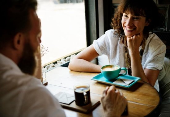 How to ask a shy guy out- woman smiling at man at a cafe.