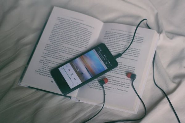 phone with earbuds on top of book in bed