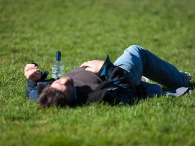 man passed out in a field with a bottle of vodka next to him