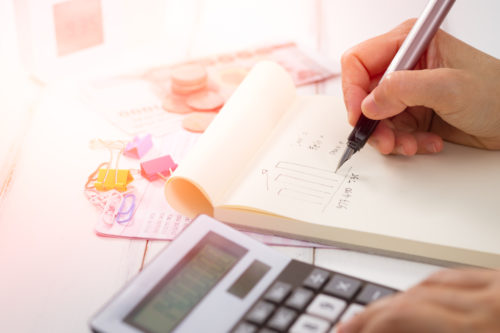 Hand writing and counting on calculator in office on wood desk about financial data analyzing, Choose focus point. In over light.