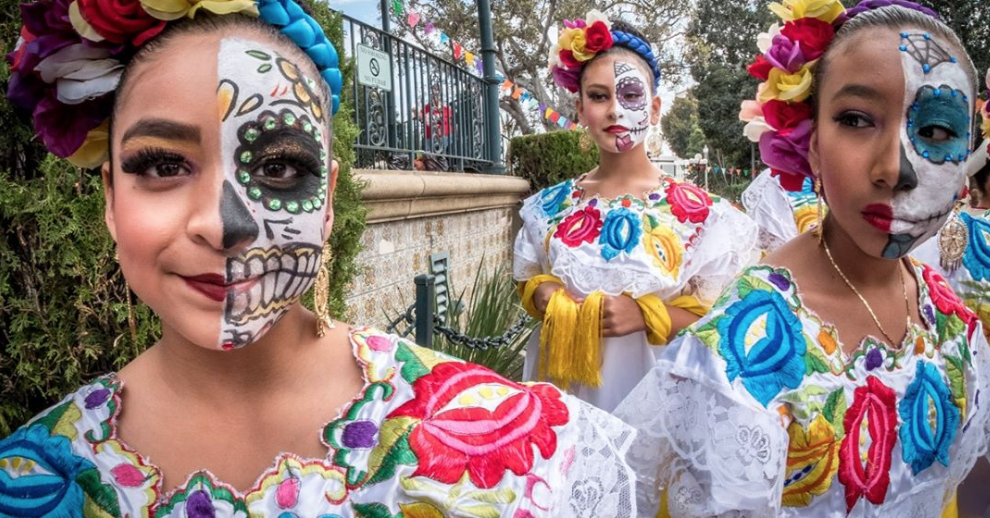 3 girsl dreseed in traditional mexican clothing and facepaint pose in front of the camera for a picture.