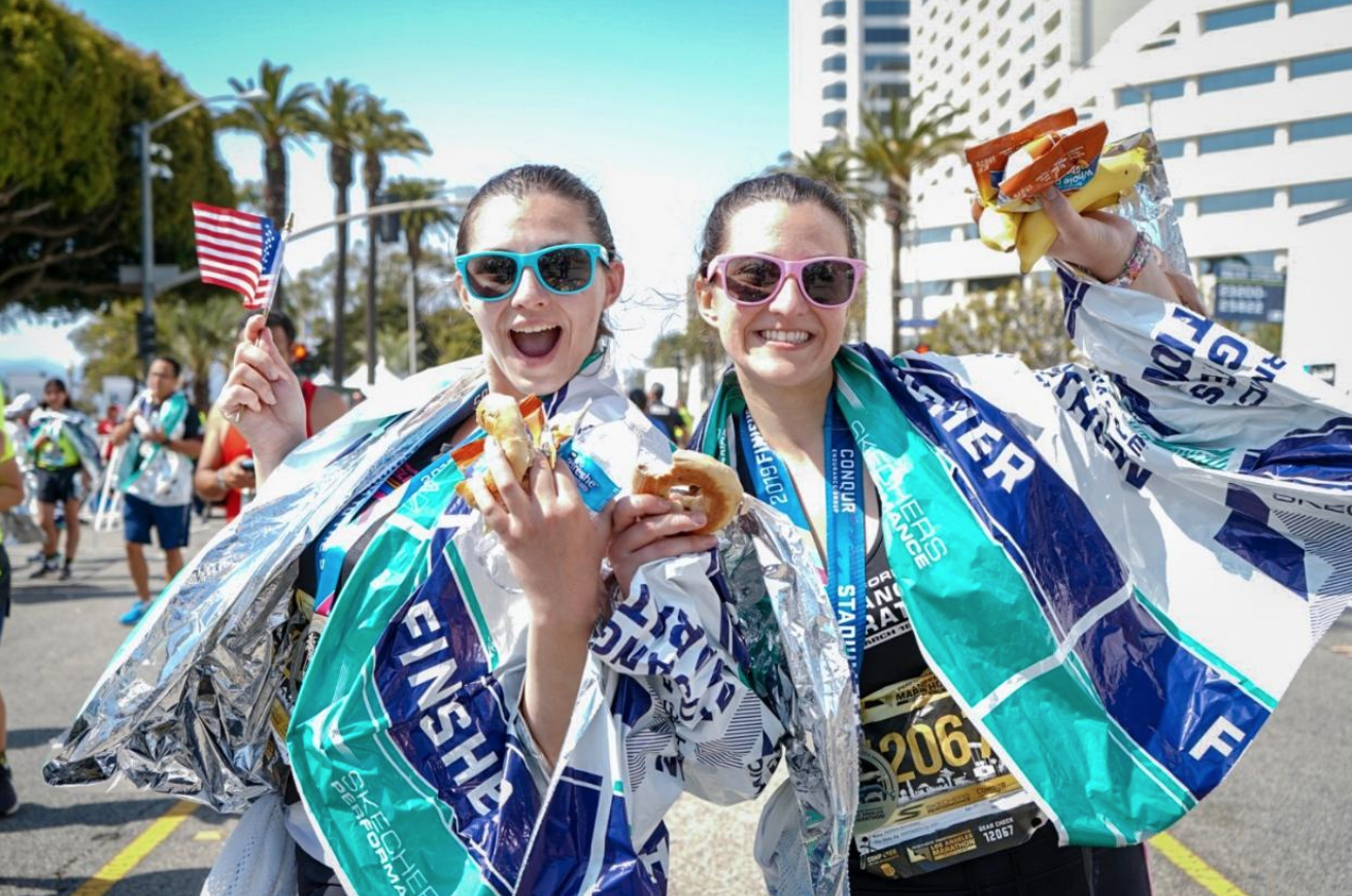 Two girls celebrate with food and medals after the marathon