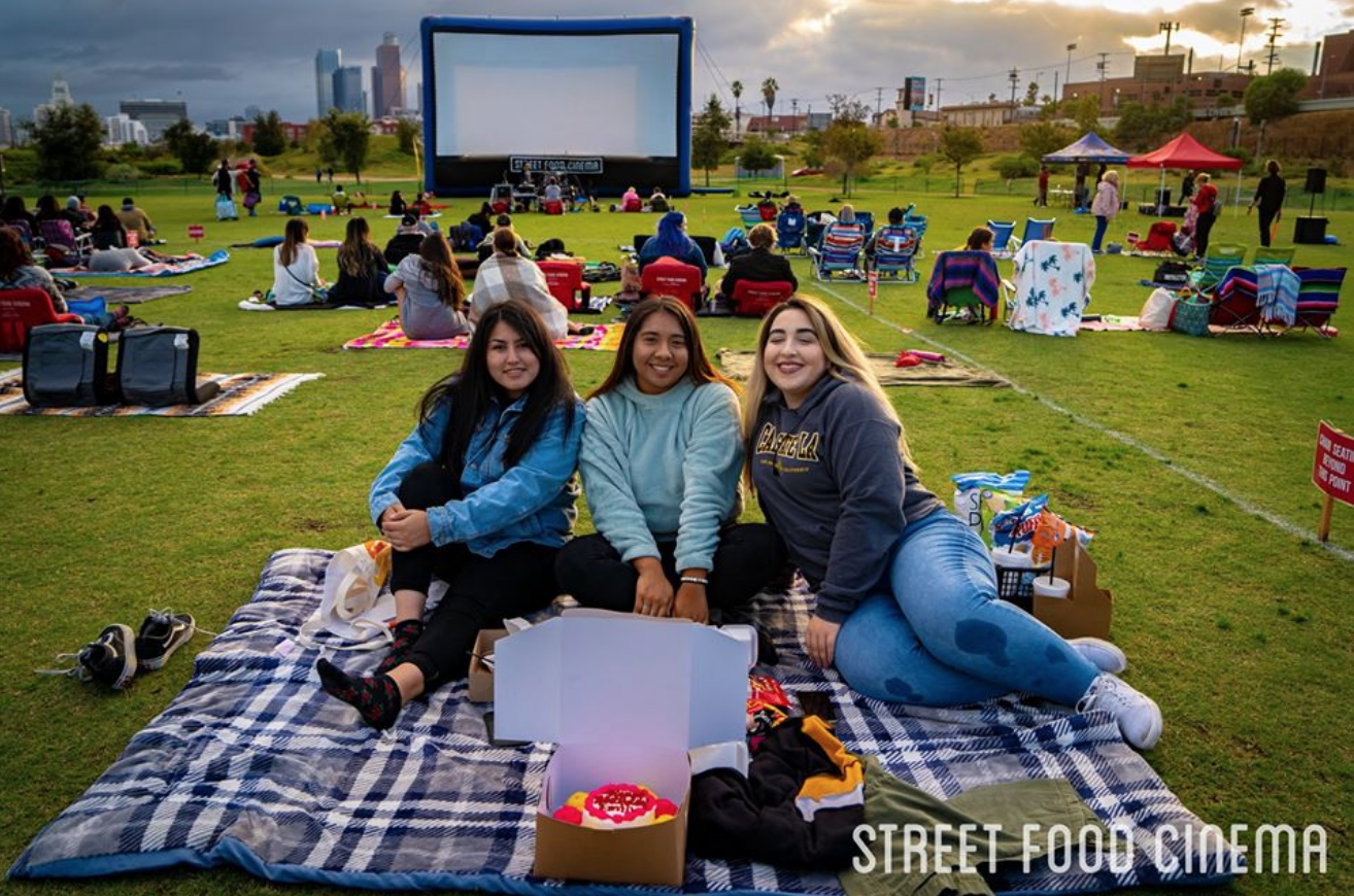 A group of young girls gather for a picture in front of a large screen at the park for a Street Food Cinema event.