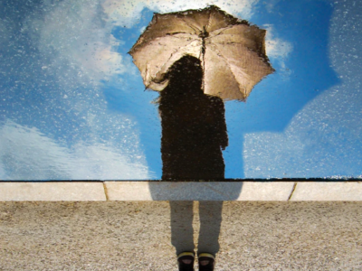 girl with umbrella looking down at her reflection in the rain