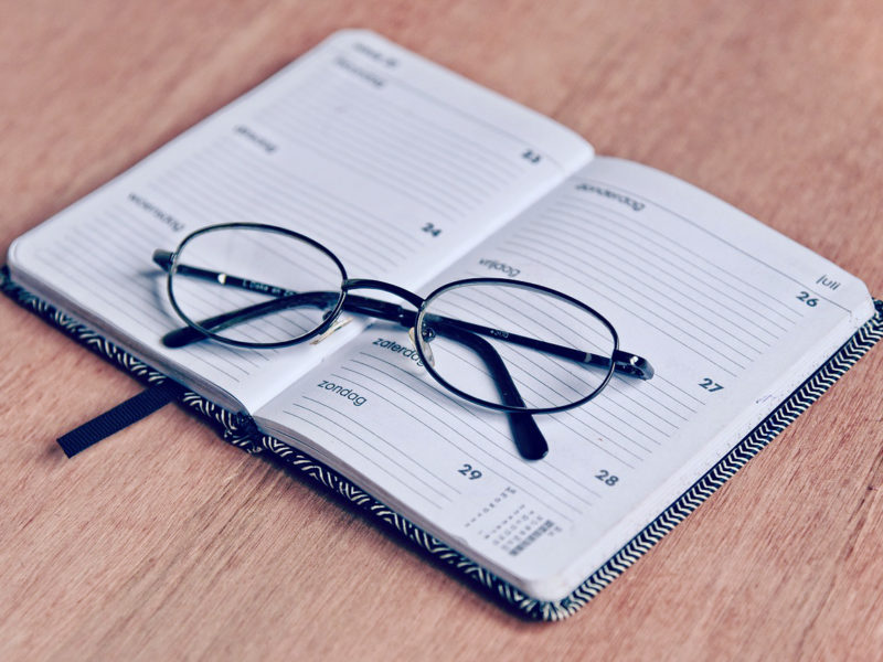 A pair of reading glasses sits atop a schedule planner notebook - making a routine when campus and businesses are closed is difficult but worth it. 