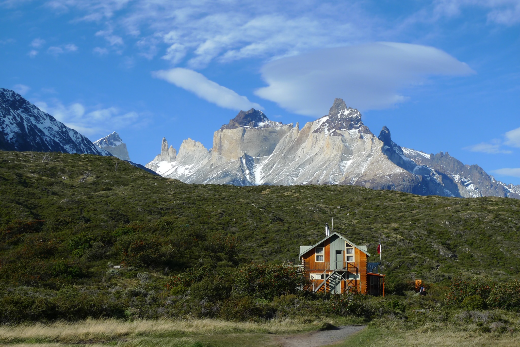 photo of Patagonia of a house in a green hillside standing before tall mountains