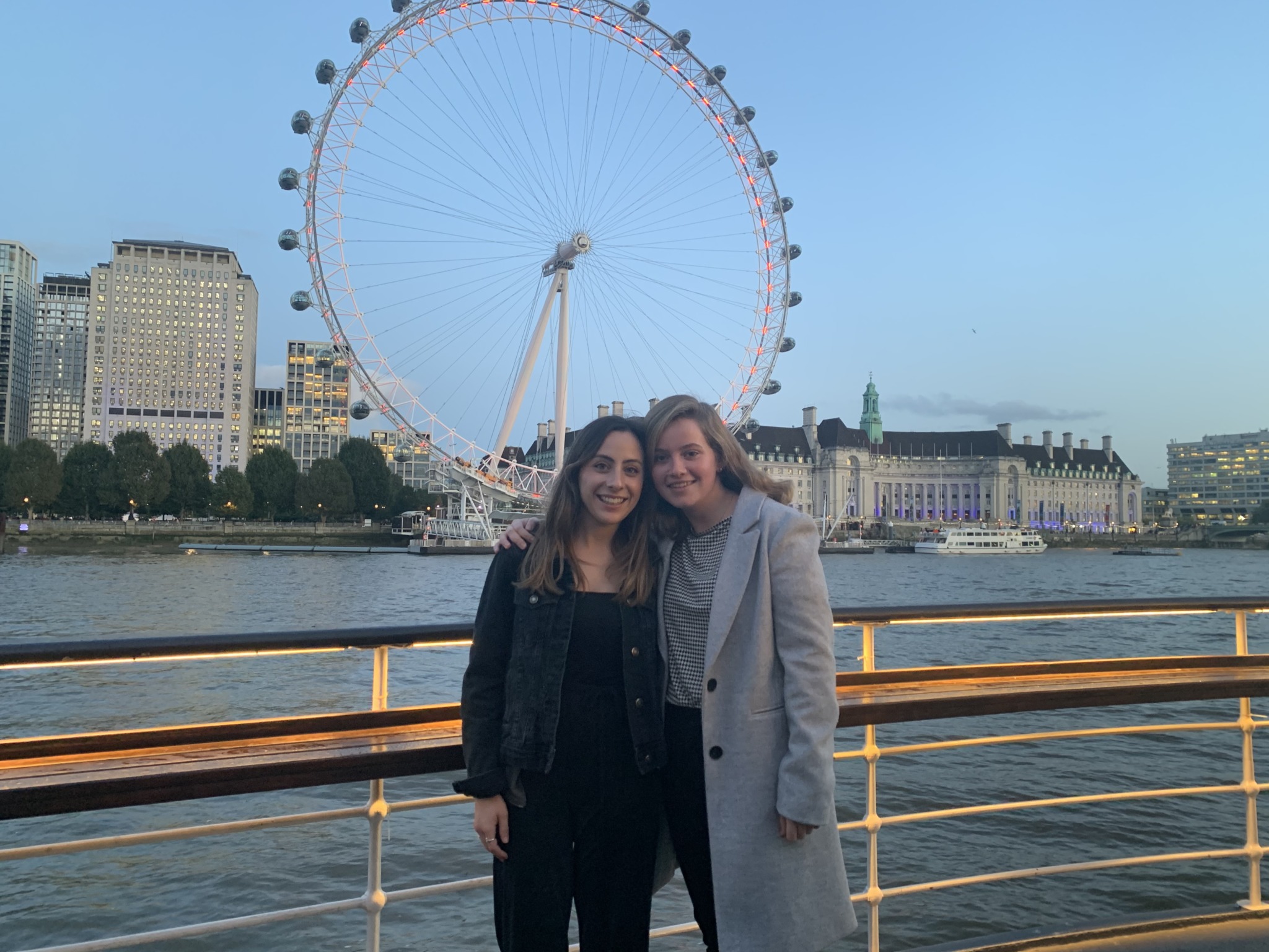 Antonia and her friend stand in front of the Thames river overlooking the London Eye