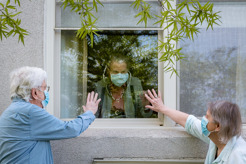 older aged people visit each other through a window during the COVID pandemic