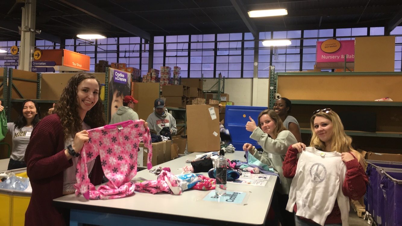 photo of college girls holding up the clothing they are sorting