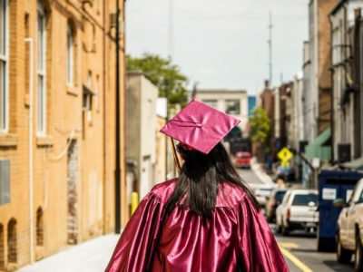 girl in graduation cap and gown standing with her back to the camera