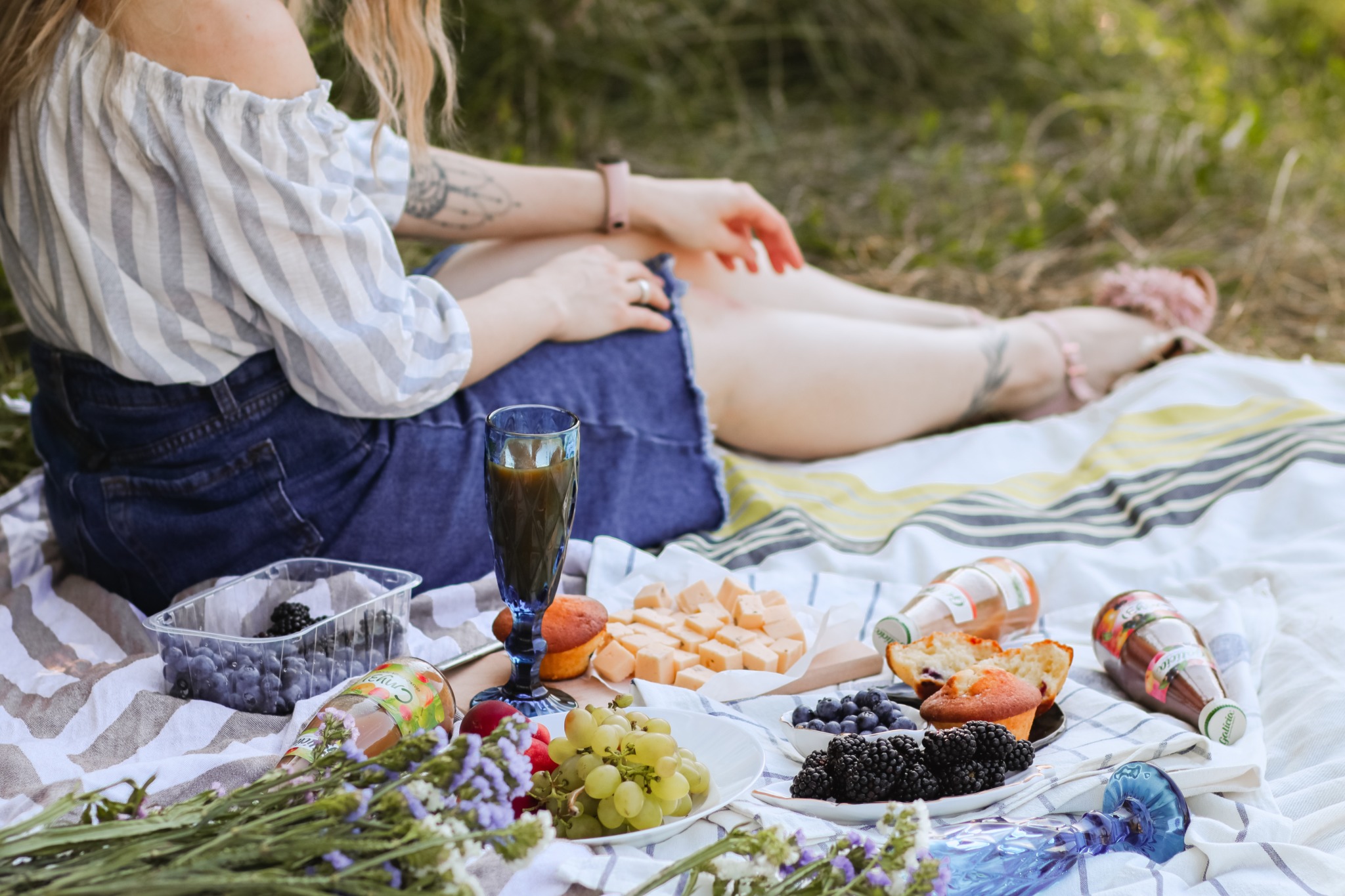 photo of a picnic laid out on a blanket with a woman sitting next to it