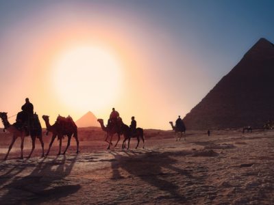 Egyptian pyramid with people riding camels at sunset