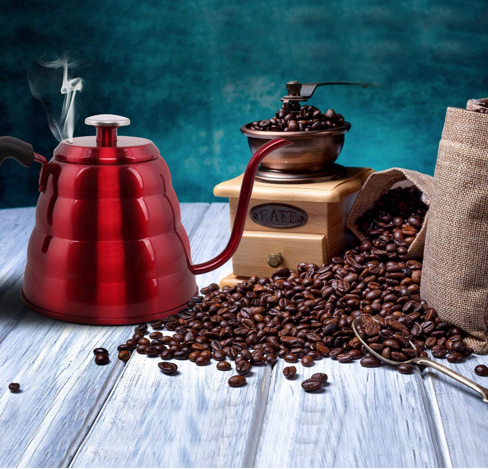 a red gooseneck kettle sitting on a table next to coffee beans