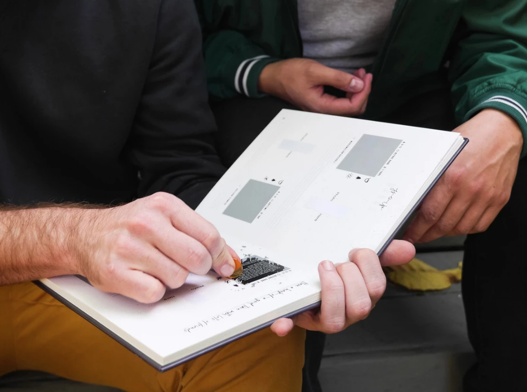 2 people scratching out challenges on the Adventure Challenge Scrapbook