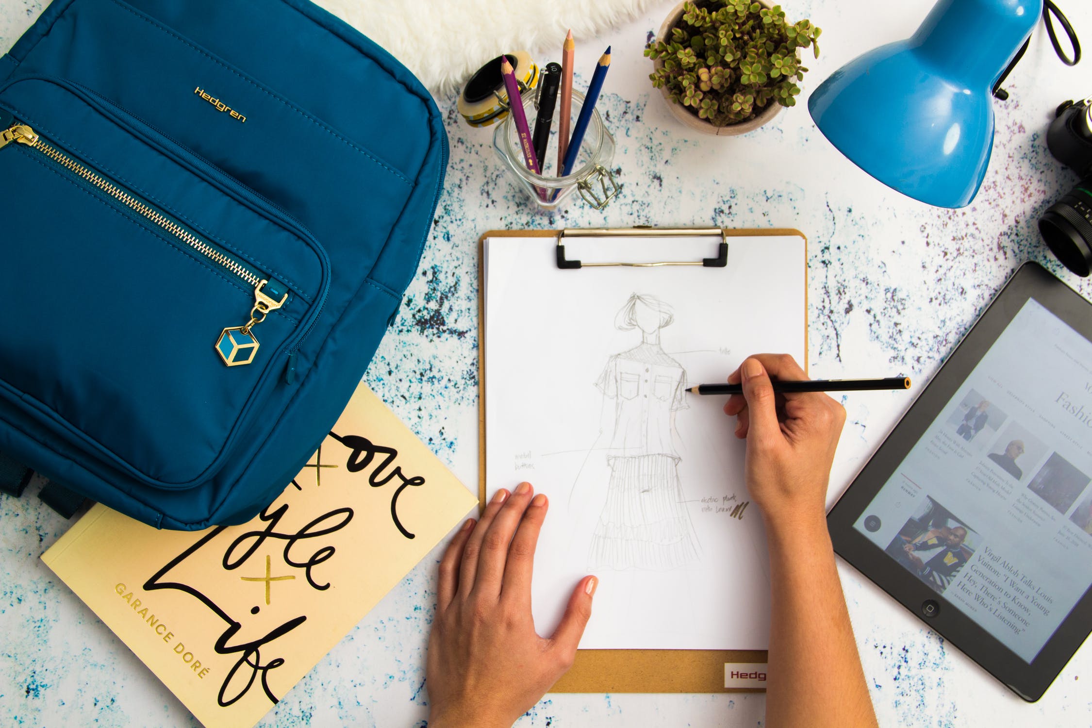 person sketching a dress with a backpack, book, lamp and iPad