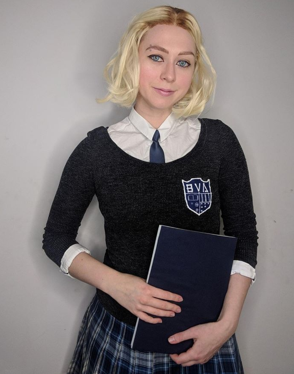 A girl dressed in a Gwen cosplay holds a book.