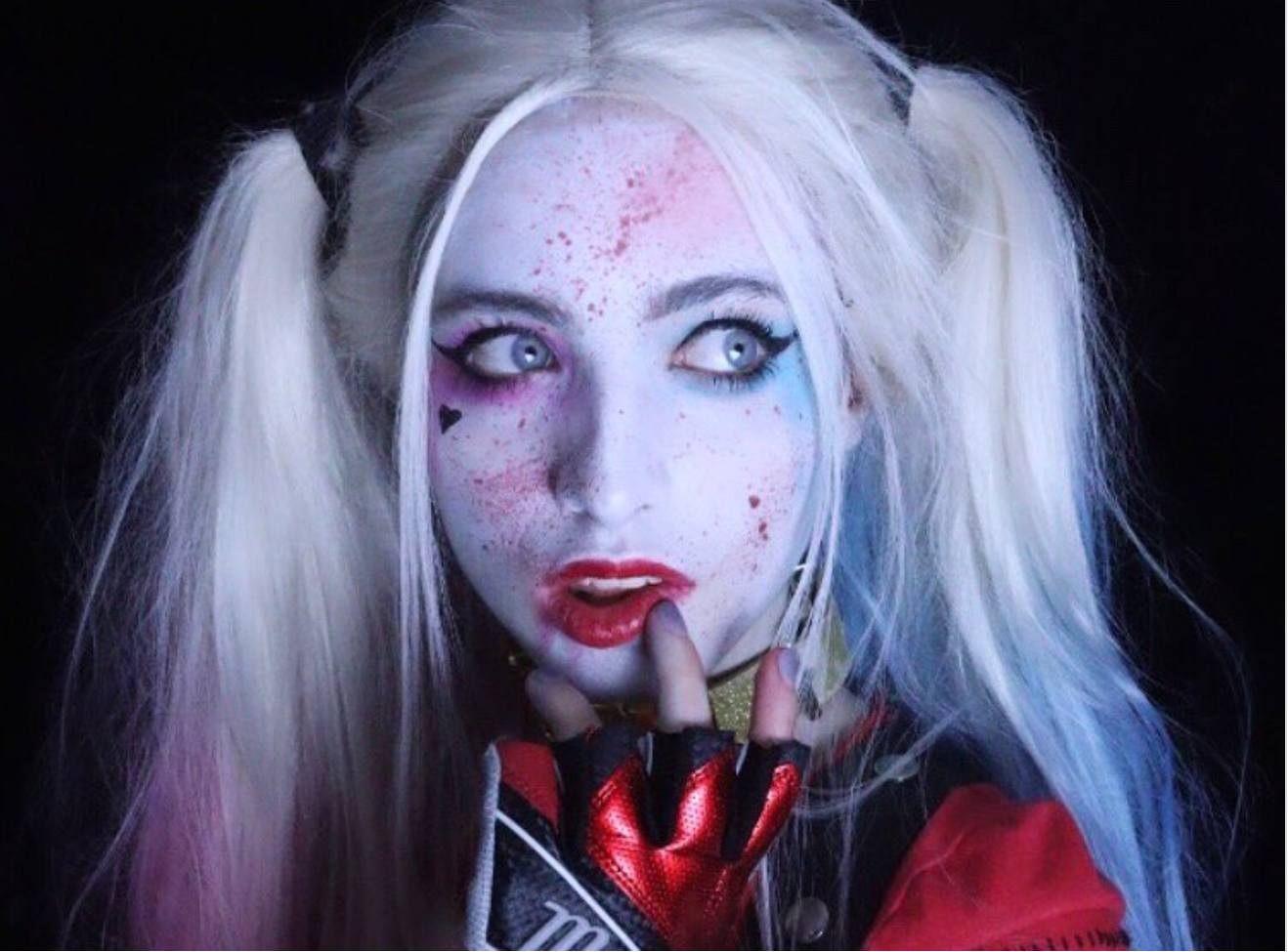 A woman is dressed in white clown makeup and pigtails as part of her Halloween costume.