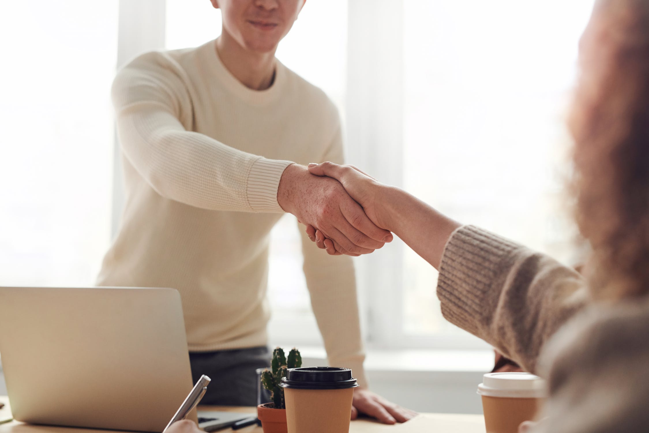 Two people shake hands over a desk.