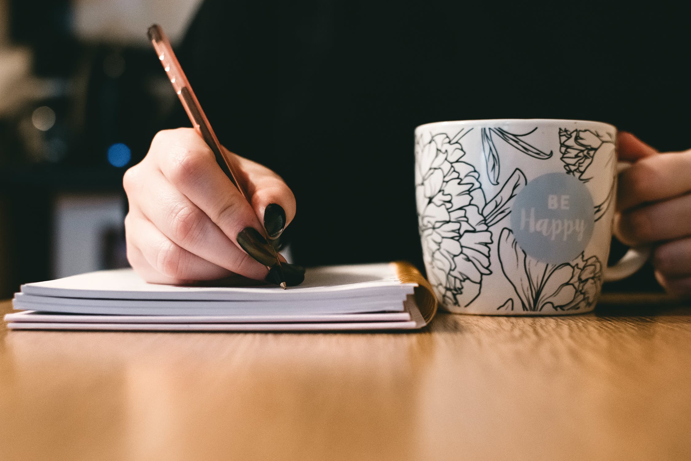 A woman writes on her notepad while holding a mug.