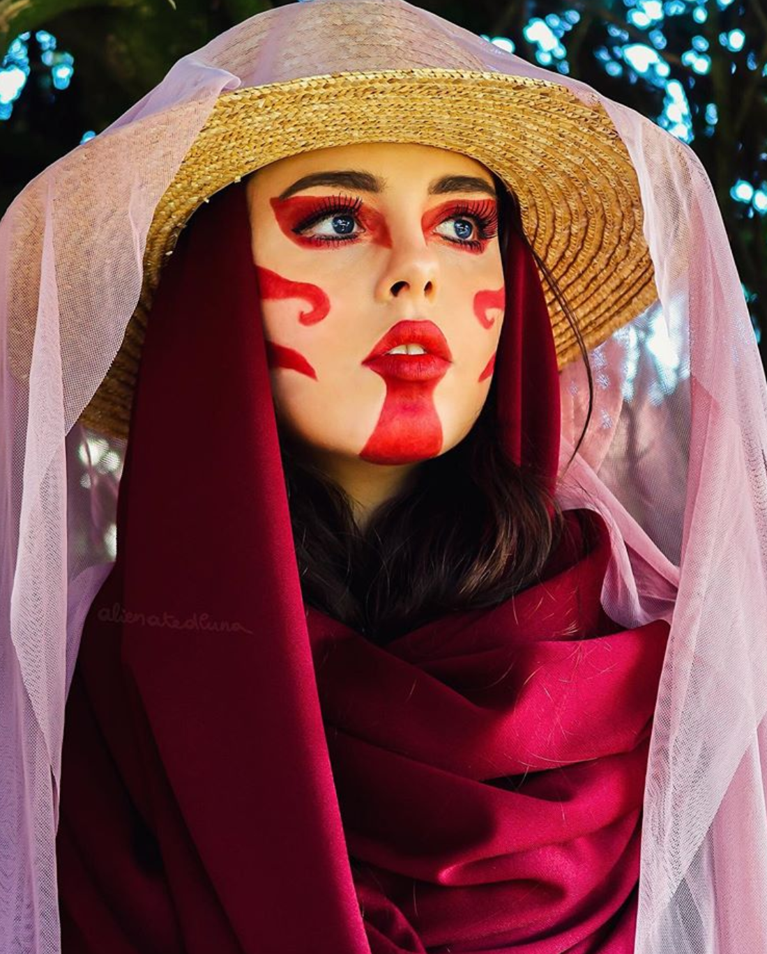 A girl in red face paint and a hat looks upwards.