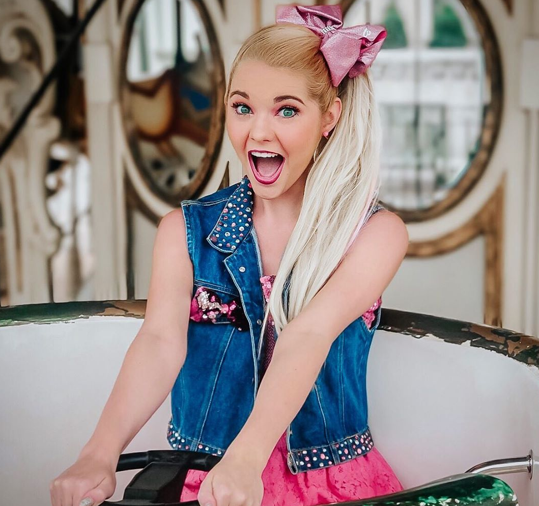 A girl with a blonde ponytail smiles while holding a steering wheel.