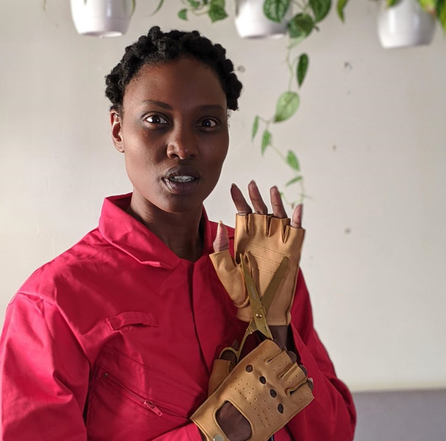 A woman holds scissors while wearing a red shirt and gloves.