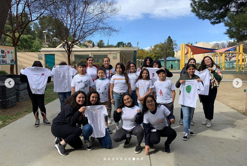 Women from LGL posing with their mentees in white t-shirts they made.