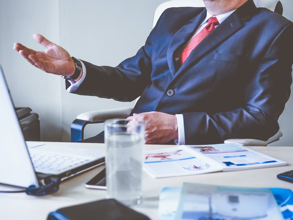 A man sits at his desk with a water and he is in a suit.