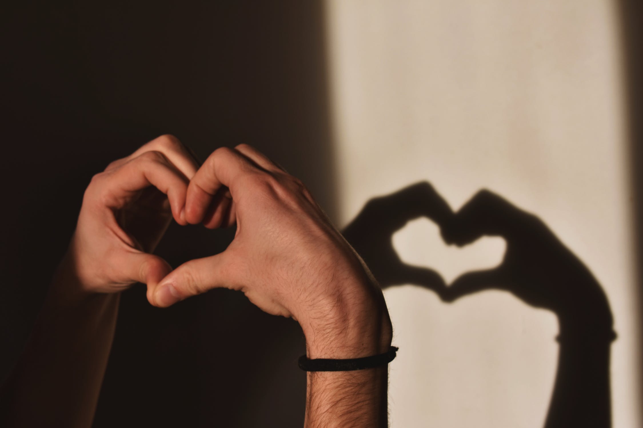 Hands making a heart shape casting a shadow on a wall.