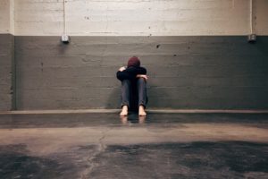 A girl with declining mental health slouches against the wall with her face buried in her arms.