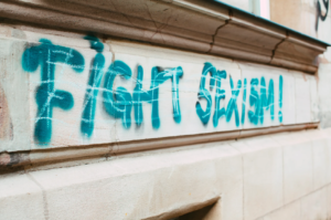 "Fight sexism" in blue spray paint on a wall because anti-sexism is pervasive part of office ethics.