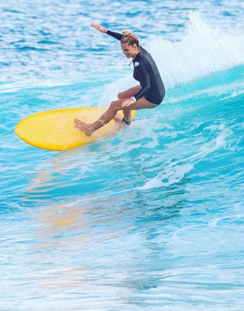 A woman in a blonde bun rides a yellow surfboard.