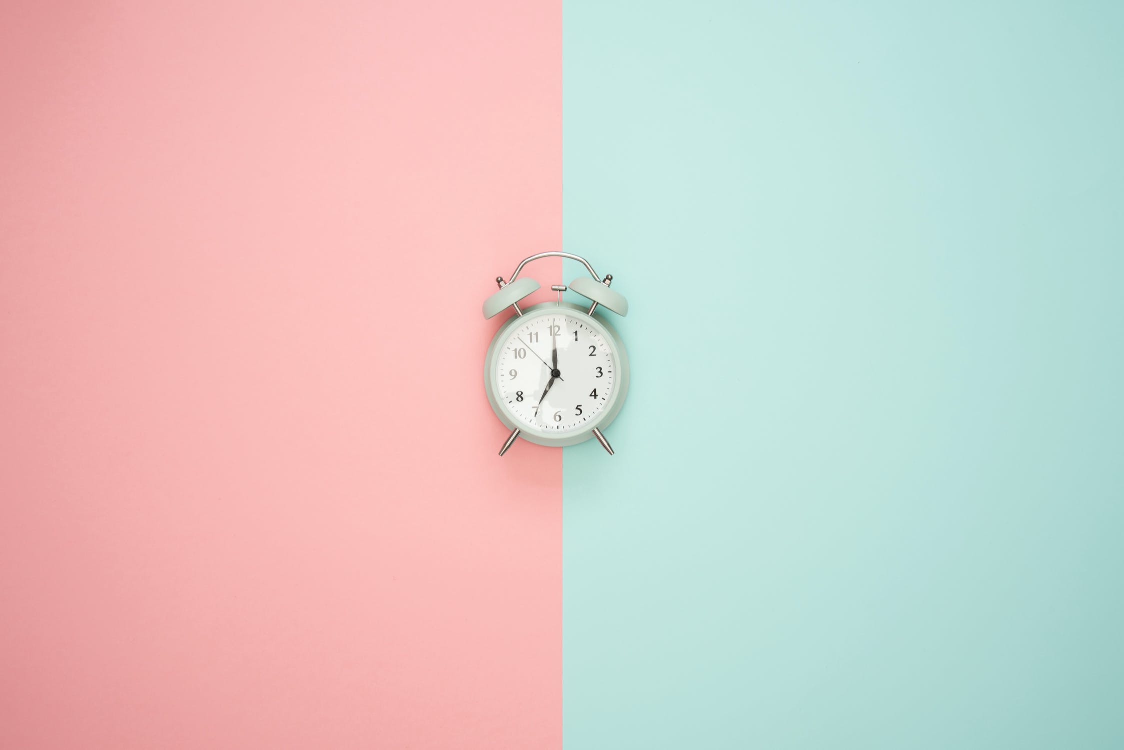 A clock sits in front of a pastel background.