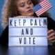 woman holding an American flag and a sign that says keep calm and vote
